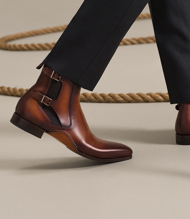 A male model steps near a rope while wearing a grey suit and Magnanni Grant Cognac boots.