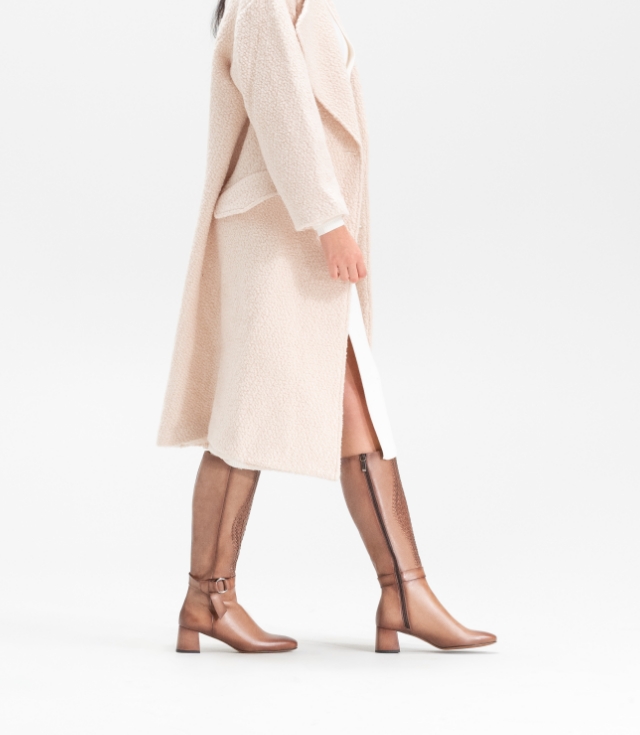 A calf-length trench coat is perfectly paired with a knee-high boot, while the woven leather patterns and rich hand-painted patina of the Aitana Woven Taupe complement this cream trench.