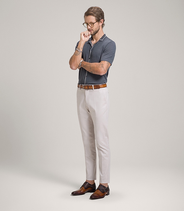 A male model stands and ponders while wearing white pants and Ondara II monk strap dress shoes in Cuero and Brown.