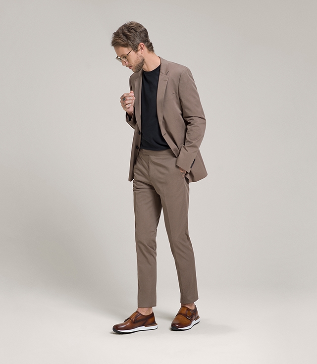 A male model wears a tan suit, black shirt, and Magnanni Orbada falcon hybrid shoes in Cognac.