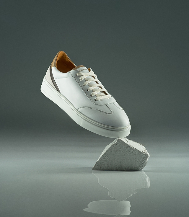 A white Magnanni Spero sneaker balances on a rock.
