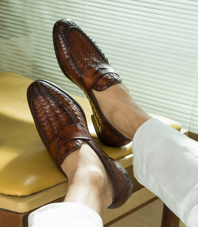 A man rests his feet on a yellow bench, wearing white pants and Magnanni Herman Cognac loafers.