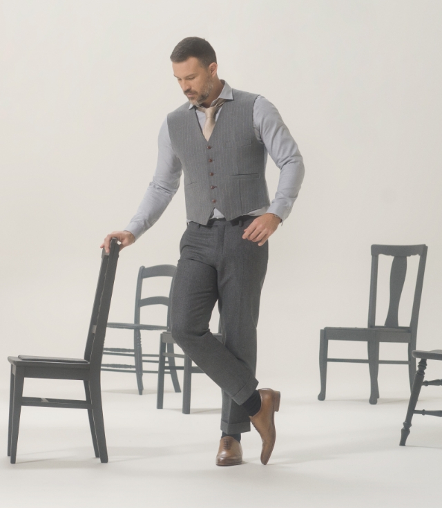 A male model rests near a group of chairs in a grey outfit and Magnanni Jonas lace ups.