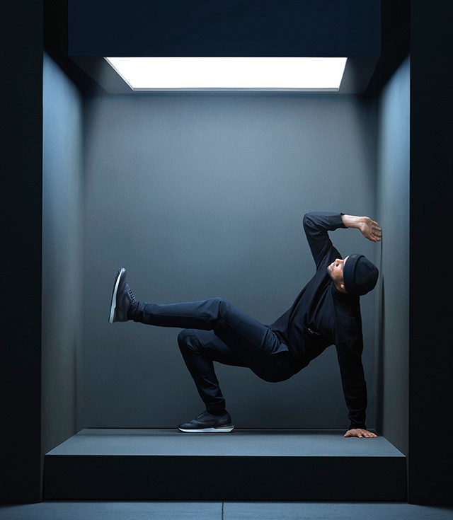 A man poses in a small room while wearing an all black outfit with Magnanni Selaya dress hybrid shoes.