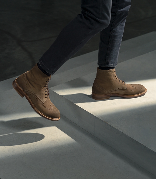 A male model steps forward on stairs while wearing dark jeans and Magnanni Teo boots.