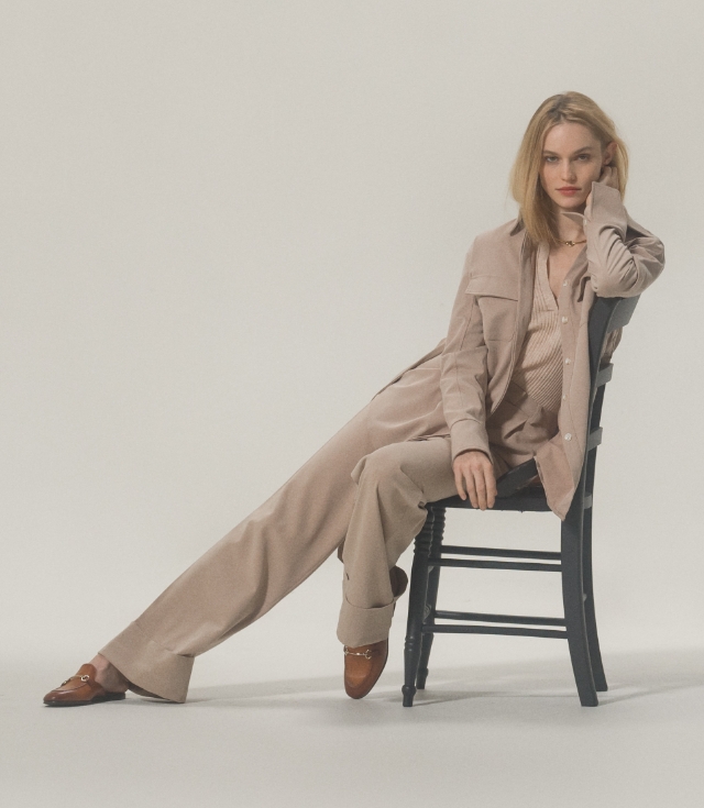 A woman sits sideways on a chair in her tan suit and Magnanni Stella V Cognac loafers.